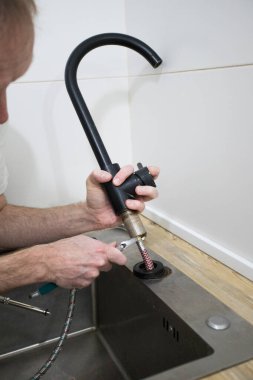 Tesisatçı mutfakta bir sorunu hallediyor.