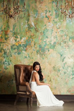 Uzun saçlı ve makyajlı genç bir kadın lüks bir iç mekanda oturuyor.