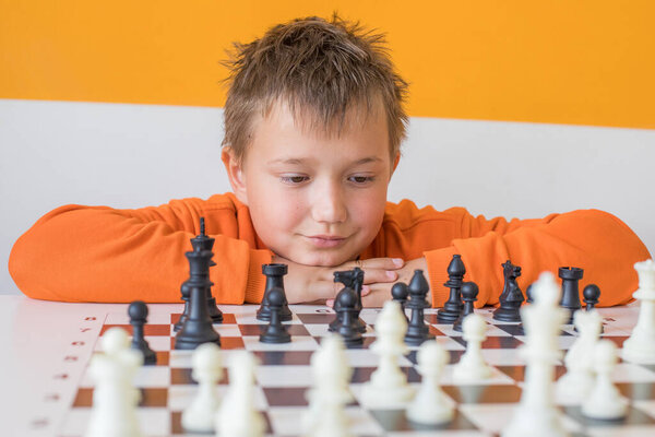 Thinking school boy student playing chess in the classroom. Child with chess indoor