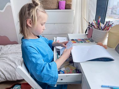 Masasında boş bir eskiz defteri olan neşeli küçük bir kız çocuğu. Ev hayatı, boş zaman aktivitesi.