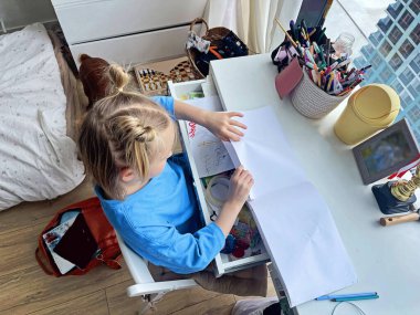Masanın üstünde boş bir eskiz defterini açmış şirin bir kız çocuğu. Ev hayatı, boş zaman aktivitesi.