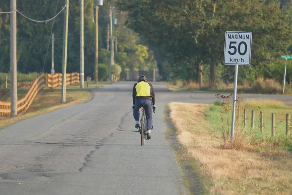 一个骑自行车的人穿着防护服在乡间路上的倒转景象 — 图库照片