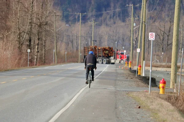 一个骑自行车的人在一辆很长的伐木卡车穿过他的小径时刹车 — 图库照片