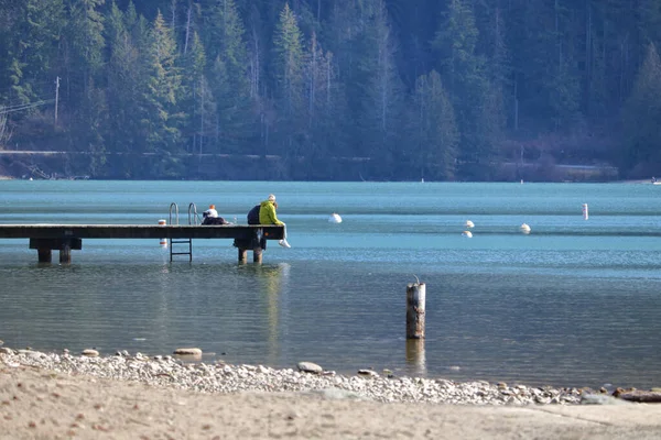 一对年轻夫妇一起坐在一个美丽湖畔的码头上 — 图库照片