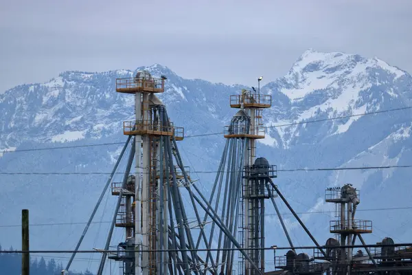Industrielle Schlote Und Schläuche Stehen Vor Einer Schneebedeckten Unberührten Bergkette lizenzfreie Stockbilder