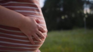 Hamile bir kadının karnının yan görüntüsünü yakından çek. Elleri hafifçe okşayarak yavaşça yürürken.