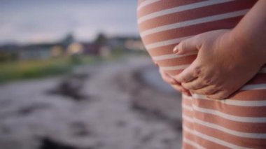 Hamile bir kadının karnını hafifçe okşayan yumuşak bir güneş ışığıyla yakın çekim.