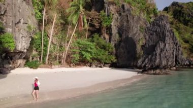 Kırmızı mayo giymiş bir kadın Entalula sahilinde tek başına yürüyor.