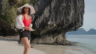 Kumsalda eğlenen bir kadın, yavaşça kameraya bakıyor.