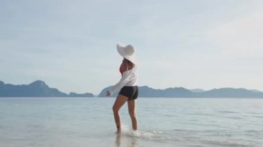 Sahilde çıplak ayakla yürüyen mutlu bir kadın.