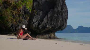 Kadın Entalula Sahili 'nde büyük bir kayanın yanında oturuyor..