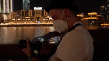 Arka planda Dubai çeşme gölü ve alışveriş merkezi olan yüz maskeli bir fotoğrafçının yakın çekimi.