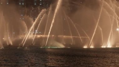 Dubai çeşmesinin sıcak ışıklarıyla su ekranını gösteren yakın çekim bir video.