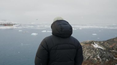 Ilulissat 'ta kış kasabasına ve buzdağlarına bakan bir adamın orta boy yakın çekimi.