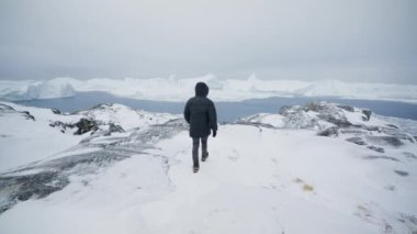Bir adamın Ilulissat 'taki karlı bir dağın tepesine ulaşma görüntüsü.
