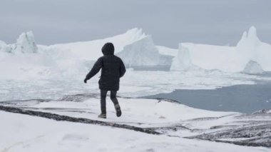 Ilulissat 'ta kar yağarken bir dağda koşan kışlık elbiseli bir adam.