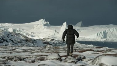 Ilulissat 'taki devasa buzullarda yürüyen bir adamın geniş açılı görüntüsü.