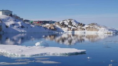 Ilulissat 'ta karlı bir kayalık dağın yakınındaki kıyı kasabasının manzarası.