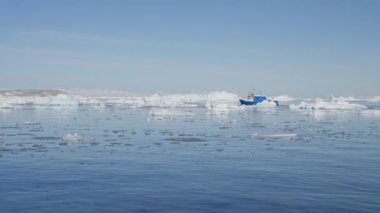 Ilulissat 'ta denizde yüzen buzdağlarının etrafında yelken açan bir teknenin geniş açılı görüntüsü.