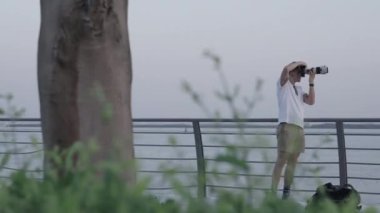 Bulanık peyzaj boyunca yayılan ve metal korkulukların yanında bir adamın görüntülerini gösteren bir video.