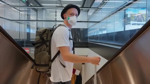 空港のエスカレーターを降りながら フェイスマスクと帽子を被った男性の乗客 — ストック動画