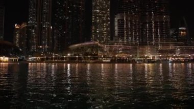 Nehir kenarındaki bir tekneden çekilen ve yakındaki nehir kenarını ve geceleri yanıp sönen güzel ışıklarla gösteren bir şehir manzarası..