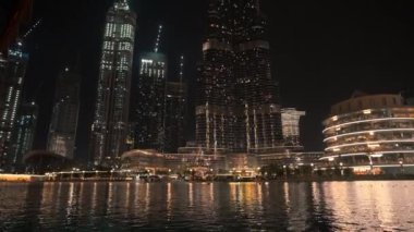 Nehir kenarından çekilen şehir manzarası gece gökyüzünde yanıp sönen güzel ışıkları olan Dubai 'nin yüksek binalarına odaklanıyor.