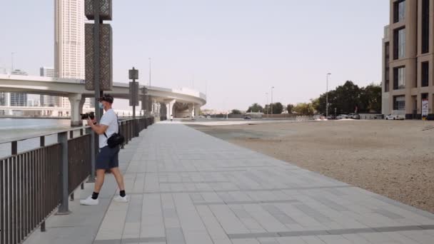 Szerokie Ujęcie Mężczyzny Robiącego Zdjęcie Budynków Drugiej Stronie Rzeki Dubaju — Wideo stockowe