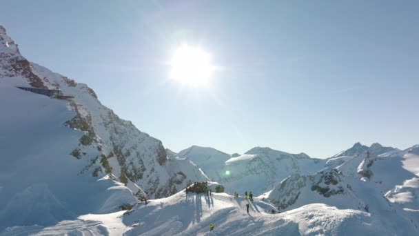 雪の山の端に集まる観光客を示すスキーリゾートで晴れた午後の空中ドローンショット — ストック動画