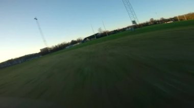 Yüksek hızlı FPV görüntüsü yeşil çimlerin üzerinde uçan ve bir ragbi sahasının kale direğinin ve çitlerinin altından geçen