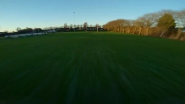 FPV insansız hava aracı gün batımında rugby sahasının altında ve üstünde hızla uçuyor.