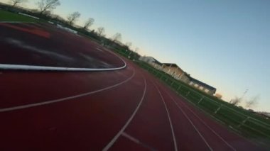 Alacakaranlıkta yarış pistinde koşan bir bayanın bordo bir kazak ve kulaklık takarken çekilmiş görüntüsü.