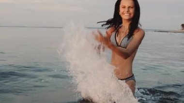 Deniz suyuyla oynayan neşeli genç bir bayanın orta boy fotoğrafı.