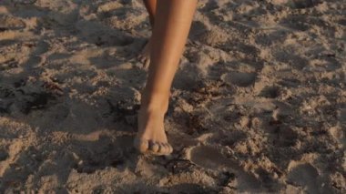 Bir insanın bacaklarının ve çıplak ayaklarının gündüz vakti yavaşça kuma basışının yakın çekimi.