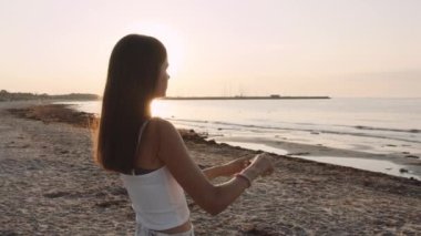 Genç bir bayanın kumsalda kamerasını kullanırken orta boy bir fotoğrafı.