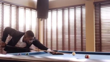 Bilardo masasındaki bilardo topuna vurmak için ıstakasını kullanan bir adamın videosu.