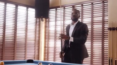 Bir adam bilardo masasına ateş ettikten sonra elini cebine soktu.