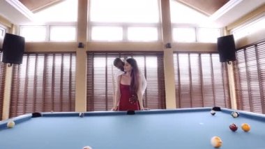 Bir adamın bilardo masasının yanında kadının sağ yanağını öperken görüntüsü.