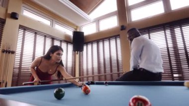 Kırmızı elbiseli bir kadının bilardo topuna vurduğunu gösteren bir video.