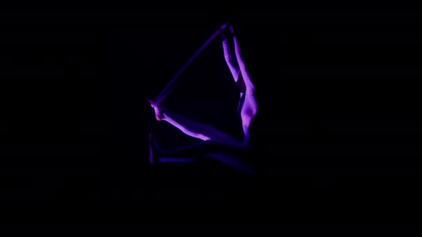 全景一个女人在一个空中钩子里做着一个分开的姿势 在一个深色的背景下 紫色的聚光灯聚焦在她的屁股上 — 图库视频影像