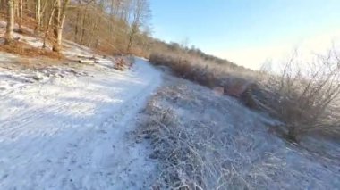 FPV yarış uçağı karlı bir zeminin üzerinde gündüz vakti bir adamın üzerinden uçuyor.