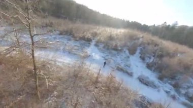 Ağaçların etrafındaki hava aracı gündüz vakti karlı bir ormandaki kulübeye giden bir adamı gösteriyor.