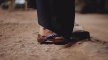 Bir mağaranın kayalık zemininde geleneksel ahşap sandaletlerle yürüyen bir kadının yakın plan fotoğrafı.
