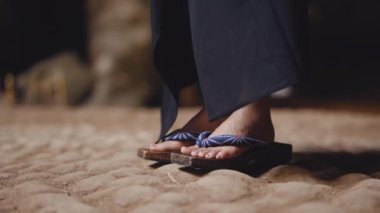 Kimono ve ahşap sandaletler giyen, kayalık bir mağaranın zemininde dikilen bir kadının yukarı doğru hareket ettiği bir eğim.
