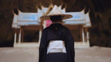 Kimono ve bambu şapkalı bir kadın, köşkünden sağ tarafına doğru yürüyor.