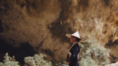 Kimono ve bambu şapkalı bir kadının el vantilatörünü tutarken, doğruca mağaraya bakarken yan görüntüsü.