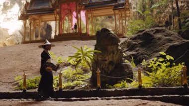 Kuha Karuha köşküne karşı kayalık yolda yürürken yelpazesini tutan bir kadının tam karesi.