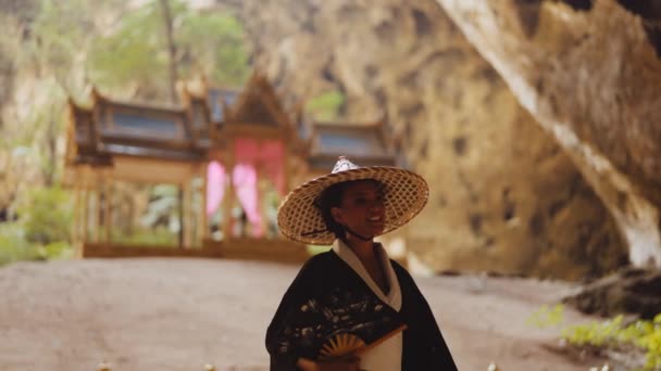 一个穿着和服 头戴竹帽 手持扇子 面对模糊的库哈 卡鲁哈亭子微笑的女人的中特写镜头 — 图库视频影像