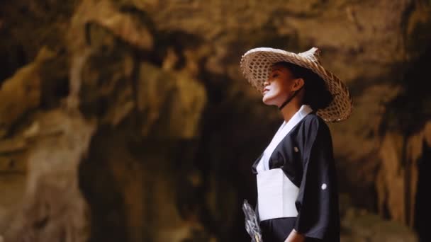 一个女人头戴和服 头戴竹帽 手持扇子 直视前方山洞的弧形照片 — 图库视频影像