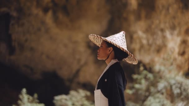 着物を着た女性と竹の帽子をかぶった女性の側面図が立っていて 洞窟をまっすぐ前を向いています — ストック動画